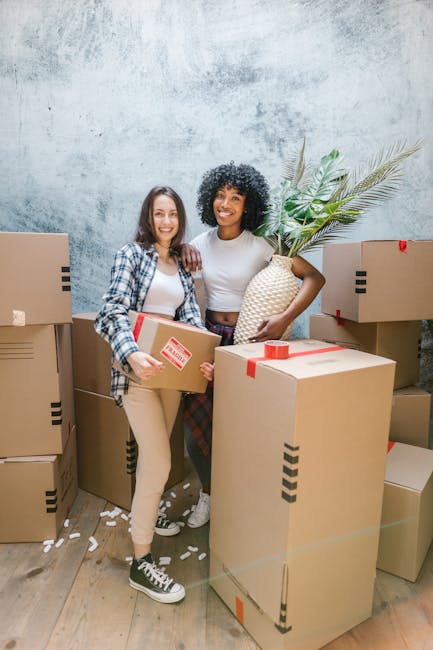 Three cardboard moving boxes stacked on a wooden floor, with the largest box at the top labeled 'STUFF' in red marker and featuring a small smiley face drawn underneath, and a smaller box below labele