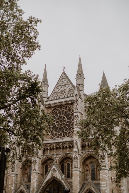A detailed view of Westminster Abbey's façade showing Gothic architecture with pointed spires and ornate stone carvings. The image captures the large, circular stained glass rose window at the center